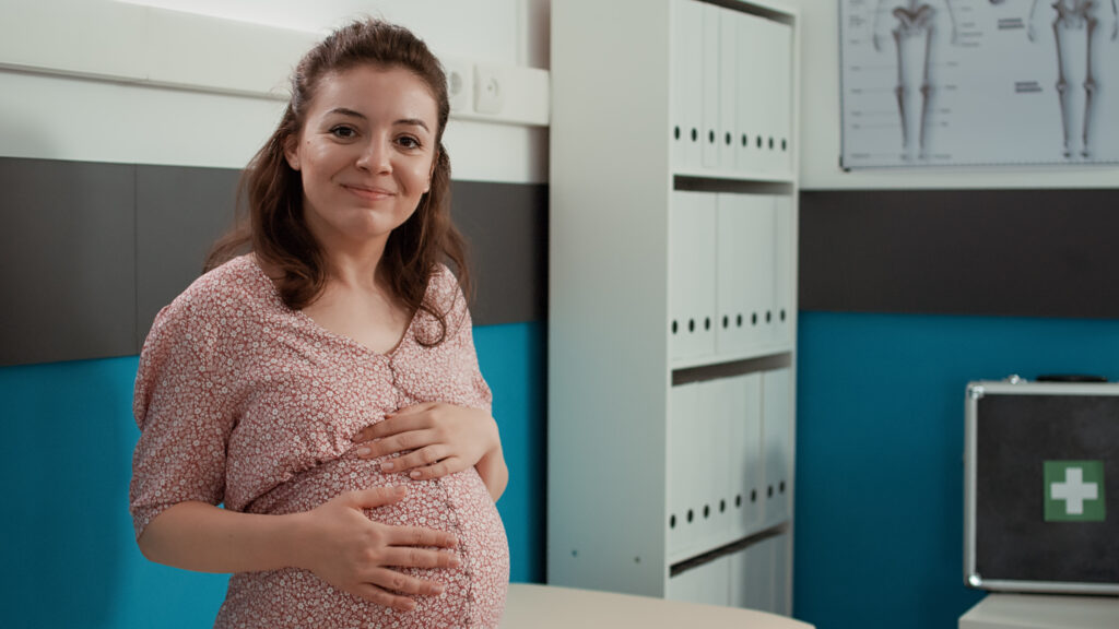 Smiling pregnant daughter standing in a medical office, representing parents learning what to do when their daughter is pregnant and how to support her.