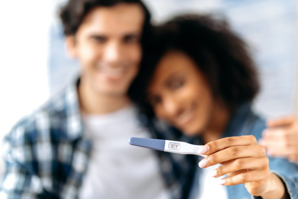 Smiling couple holding a positive pregnancy test, representing support and shared decision-making during an unplanned pregnancy